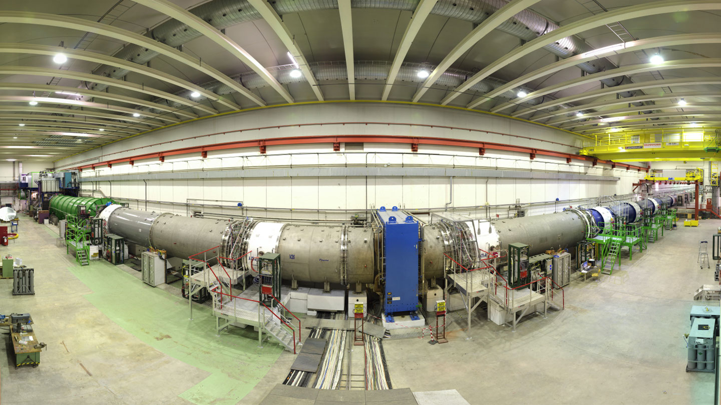 A long, cylindrical experiment of particle physics appears in a wide -angle image.