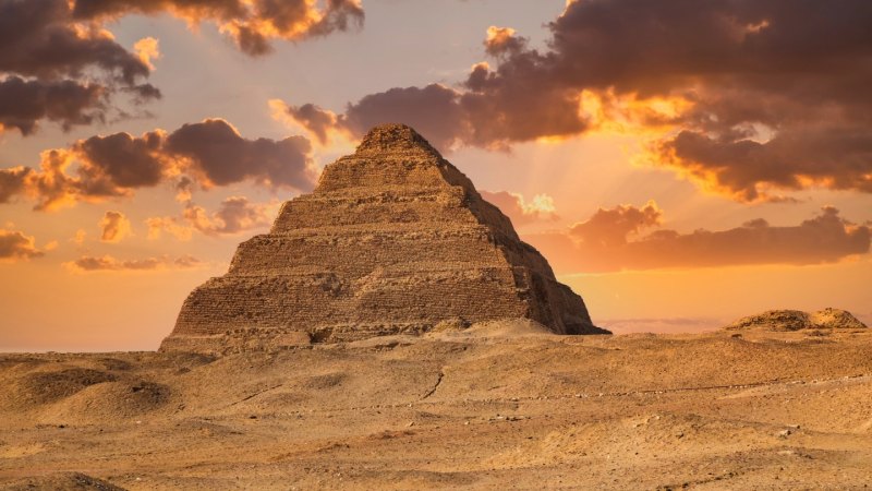 The Egyptian king Djoser's pyramid rises on a sandy landscape, while the sun -colored clouds throw a golden glow on stage.